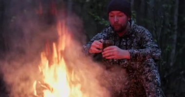 Ormandaki ateşin yanında sıcak çay içen bir adam. İnsan yaz aylarında orman yangınına bakar ve doğada çay içer. Yalnız gezgin ateşin yanında oturur ve alacakaranlıkta bir fincan kahveyle dinlenir.. 