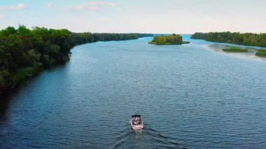 İnsansız hava aracı, gün batımında içinde insanlar varken, yavaş bir sürat teknesiyle nehrin üzerinde uçuyor. Göldeki sürat teknesini grup insanlarla birlikte kullanmanın havadan görüntüsü. Aile küçük bir yatta dinleniyor..