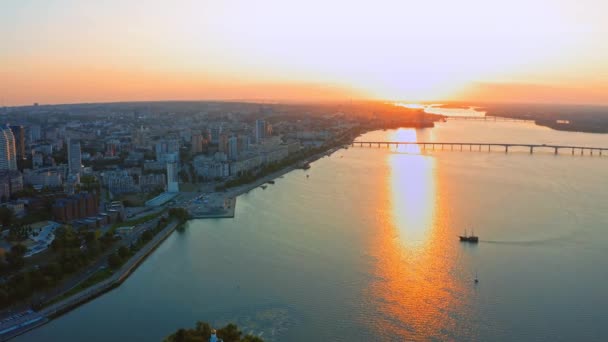 広い川 長い橋と大きな建物と美しい都市環境の上に空中ビュー 日没中 夕日の川と美しい街の風景の上を飛ぶドローン — ストック動画