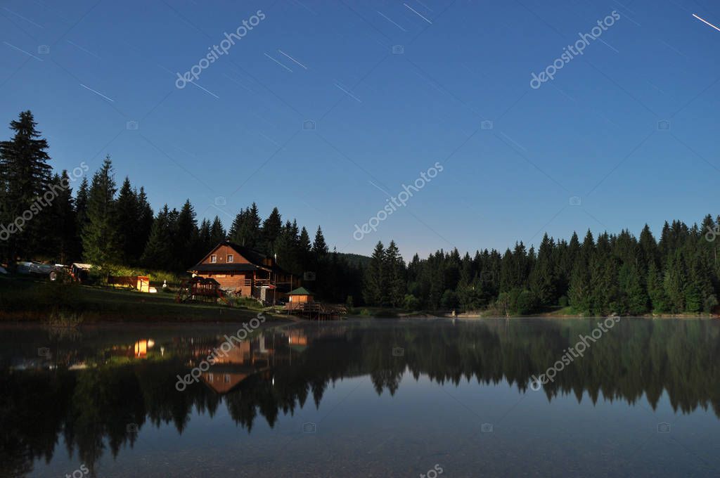 Forest and cottage reflecting in the lake at night