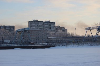 Soğuk bir akşamda, bulutlu gökyüzünde günbatımı endüstriyel liman ve nehir setinin arka planında.