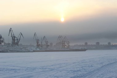 Soğuk bir kış gününde gün batımında bir kargo limanı ve donmuş bir nehre karşı
