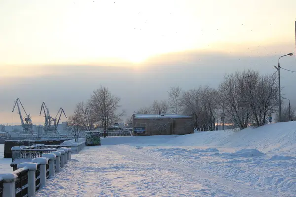 Soğuk bir akşamda, bulutlu gökyüzünde günbatımı endüstriyel liman ve nehir setinin arka planında.