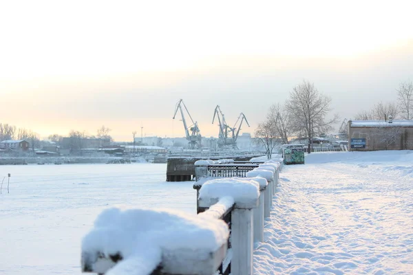Soğuk bir akşamda, bulutlu gökyüzünde günbatımı endüstriyel liman ve nehir setinin arka planında.