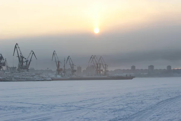 Soğuk bir kış gününde gün batımında bir kargo limanı ve donmuş bir nehre karşı
