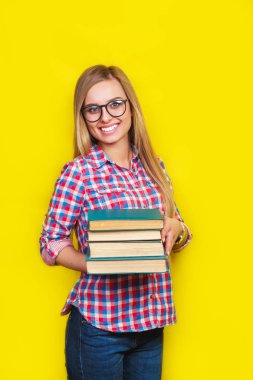 Genç şık öğrenci gülümseyen gözlük ve rahat parlak kıyafeti sarı arka plan kitapları ile ayakta
