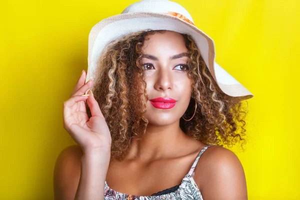 Beauty portrait of young african american girl with afro hairstyle in summer hat. Girl posing on yellow background, looking at camera. — Stock Photo, Image