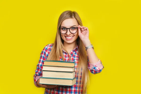 안경 및 캐주얼 밝은 옷에 노란색 배경에 책으로 서 젊은 세련 된 학생을 웃 고 — 스톡 사진