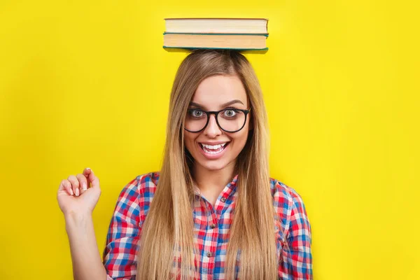 그녀의 머리에 책을 들고 안경에 젊은 여자. 노란 배경에 서 서 웃 고 있는 젊은 세련 된 학생 — 스톡 사진