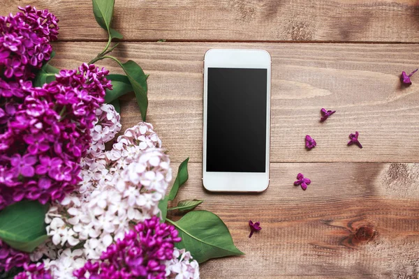 Boeket van lila bloemen op houten planken met mobiele telefoon. Bovenaanzicht — Stockfoto