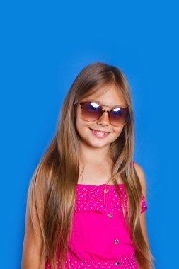 Pembe elbiseli, güneş gözlüğü ve şapka mavi zemin üzerine genç Sevimli Kız portresi. Yaz tatil ve seyahat kavramı