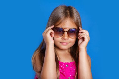 Pembe elbiseli, güneş gözlüğü ve şapka mavi zemin üzerine genç Sevimli Kız portresi. Yaz tatil ve seyahat kavramı