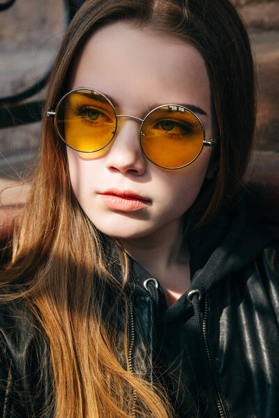 beautiful fashionable teenager girl with long hair in yellow sunglasses in city, Street fashion kid,