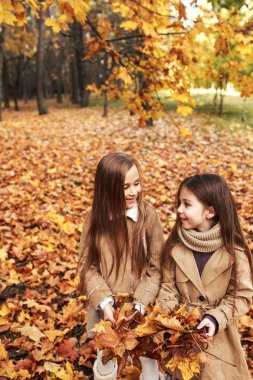 İki küçük kız oynar Park Sonbahar yaprakları