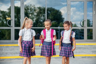 İlköğretim Okulu öğrencileri. Açık havada bina yakınındaki sırt çantaları kızlarla. Ders başlangıcı. Sonbaharın ilk günü.