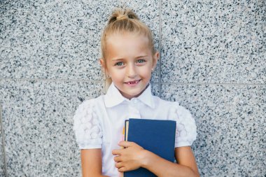 Elinde kitapla ilkokul öğrencisi. Açık hava binasının yakınında sırt çantalı bir kız. Dersler başlıyor. Sonbaharın ilk günü.