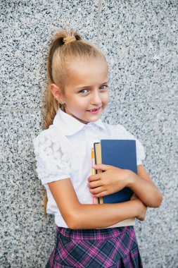 Elinde kitapla ilkokul öğrencisi. Açık hava binasının yakınında sırt çantalı bir kız. Dersler başlıyor. Sonbaharın ilk günü.