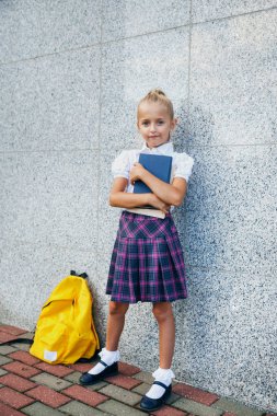 Elinde kitapla ilkokul öğrencisi. Açık hava binasının yakınında sırt çantalı bir kız. Dersler başlıyor. Sonbaharın ilk günü.