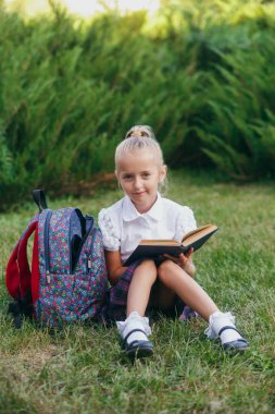 küçük kız çim ve okuma kitap üzerinde oturuyor. Öğrenciler İlköğretim Okulu.