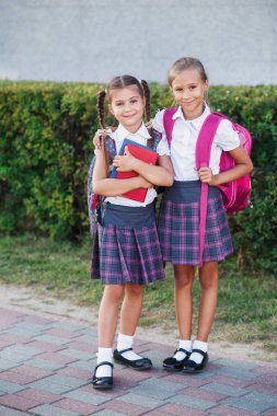 İlköğretim Okulu öğrencileri. Sırt çantaları ve açık havada bina yakınındaki kitaplar kızlarla. Ders başlangıcı. Sonbaharın ilk günü.