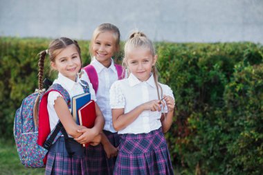 İlköğretim Okulu öğrencileri. Sırt çantaları ve açık havada bina yakınındaki kitaplar kızlarla. Ders başlangıcı. Sonbaharın ilk günü.