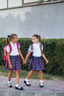 İlköğretim Okulu öğrencileri. Açık havada bina yakınındaki sırt çantaları kızlarla. Ders başlangıcı. Sonbaharın ilk günü.