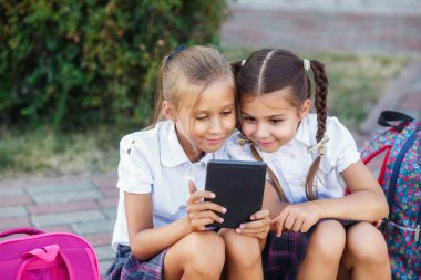 Genç kızlar bir ebook okuma. İlköğretim Okulu öğrencileri. Açık havada bina yakınındaki sırt çantaları kızlarla