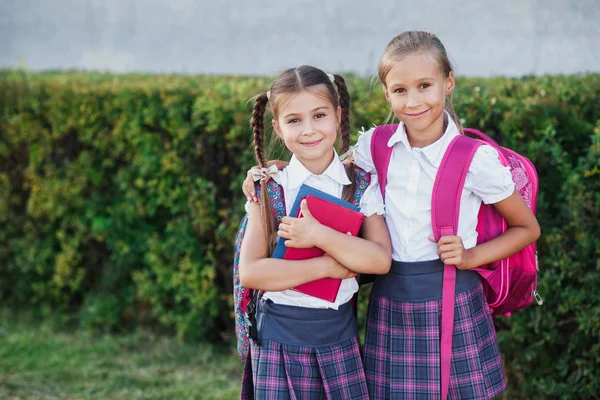 Pupils of primary school. Girls with backpacks and books near building outdoors. Beginning of lessons. First day of fall.