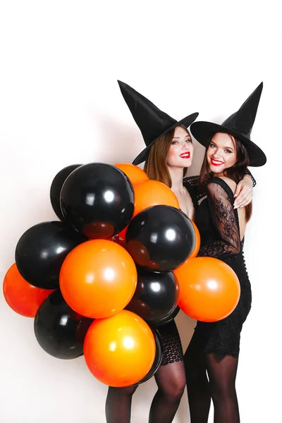 ブラックでエレガントな つのセクシーな女性は 白い背景の上パーティーにオレンジと黒の風船でハロウィーンの衣装を魔女します — ストック写真