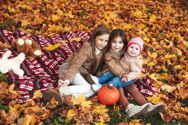 Three happy little girls havinh fun playing with fallen golden leaves