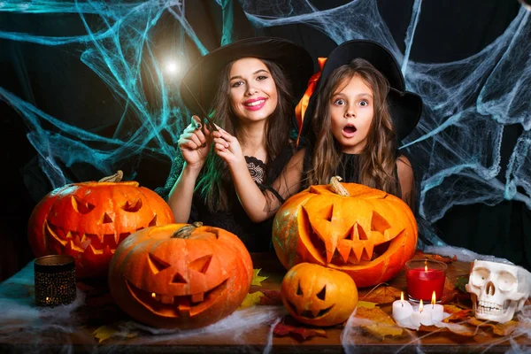 Cadılar Bayramınız Kutlu Olsun. Güzel beyaz anne ve kızı cadı kostümleri örümcek ağı üzerinde siyah stüdyo arka plan üzerinde halloween balkabağı kavanoz için sihirli değnek ile büyü kullanmaktan zevk. — Stok fotoğraf