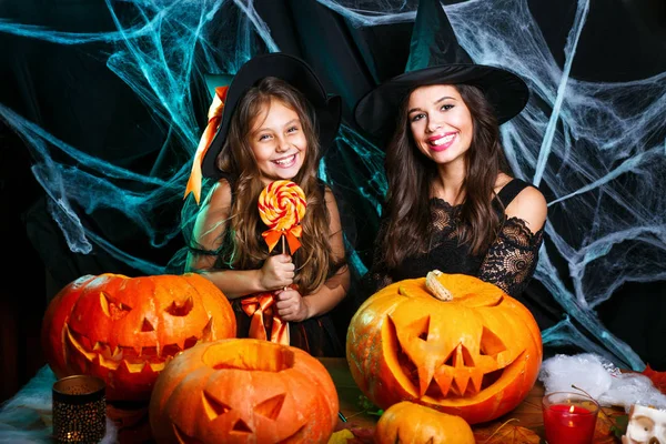 Vrolijke Halloween. Mooie Kaukasische moeder en haar dochter in heks kostuums Halloween vieren met Halloween snoep en zoet over spinnenweb — Stockfoto