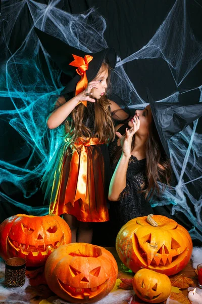 Halloween Concept - close-up mooie Kaukasische moeder en haar dochter in heks kostuums vieren Halloween poseren met gebogen pompoenen over spinnenweb — Stockfoto