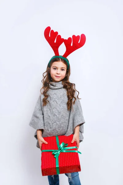 Feliz niña sonriente con caja de regalo de Navidad mirando en la cámara. Concepto de Navidad. Sonriente chica divertida en cuernos de ciervo en el estudio . —  Fotos de Stock