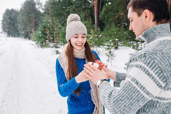 Jovem casal segurando coração de neve na floresta de inverno. Mãos em mitenes tricotadas com o coração da neve no dia de inverno. Conceito de amor. Dia dos namorados fundo . — Fotografia de Stock