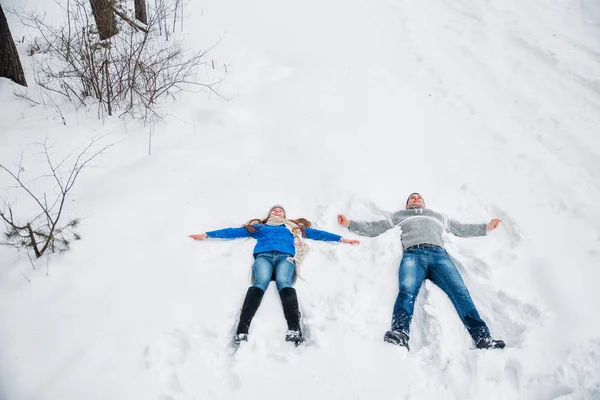 Casal deitado na neve fazendo Snow Angel. Férias inverno — Fotografia de Stock