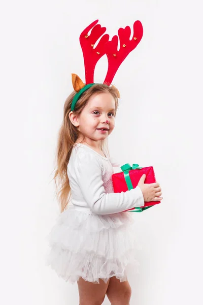 Bebé de Navidad en cuernos de ciervo sosteniendo una caja de regalo roja sobre fondo blanco. Tiempo de Navidad —  Fotos de Stock