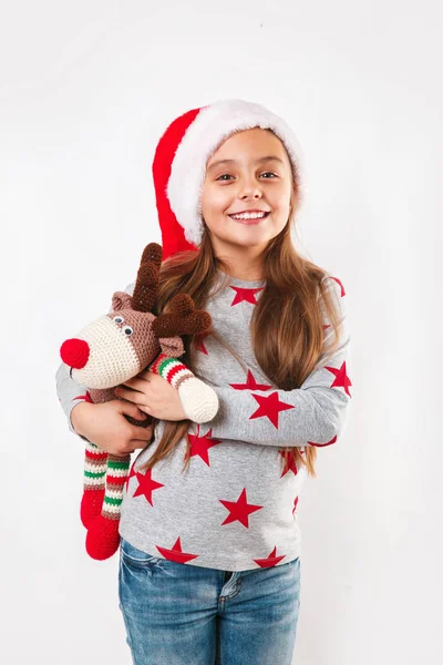 Симпатичный маленький ребенок в шляпе Санты с вязаным оленем. Девушка смеется и наслаждается подарком. Концепция Рождества — стоковое фото