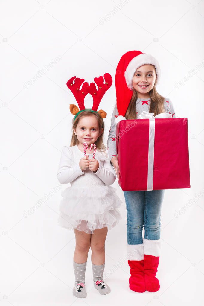 Two happy little smiling kids in Santa hat and deer horns with big christmas gift box and sweets. Christmas time