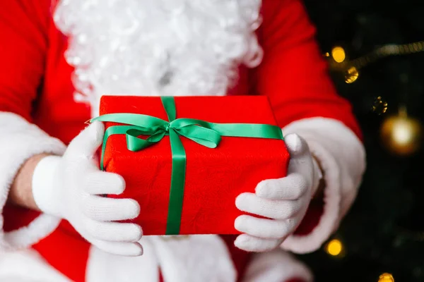 Piros ajándék Mikulás kezében karácsonyi háttér közelében — Stock Fotó