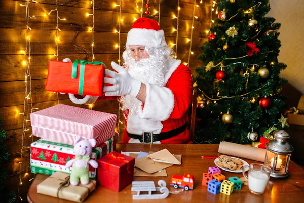 Frohe Weihnachten und frohe Feiertage. Weihnachtsmann bereitet Geschenke für Kinder zu Weihnachten am heimischen Schreibtisch vor. — Stockfoto