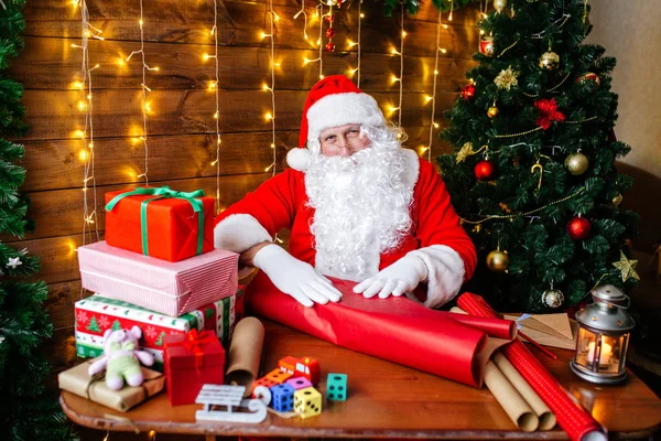 God jul och god jul. Santa Clause förbereder presenter till barn för Xmas vid skrivbord hemma. — Stockfoto