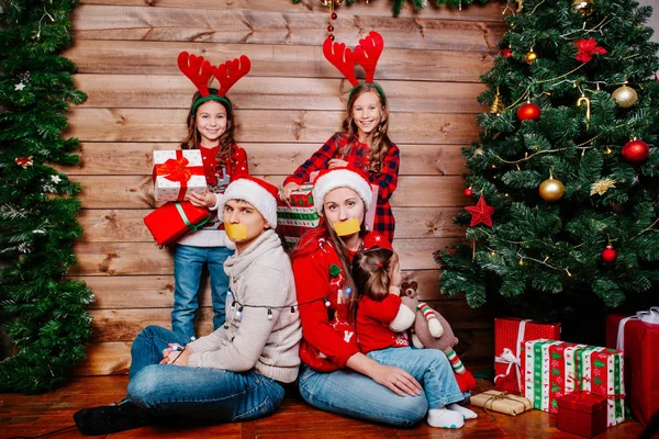 Bad kids and father and mother tied up with garland near Christmas tree at home