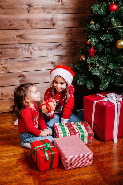 Feliz Navidad y Felices Fiestas. Dos niñas lindo niño con regalo cajas de regalo cerca del árbol de interior —  Fotos de Stock