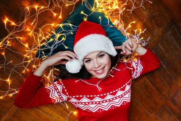 Primer plano retrato de la mujer en el sombrero de Santa envuelto en luces de Navidad divertirse y acostarse en el suelo — Foto de Stock