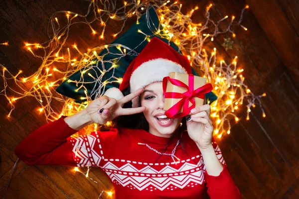 Primer plano retrato de la mujer en el sombrero de Santa envuelto en luces de Navidad divertirse y acostarse en el suelo — Foto de Stock