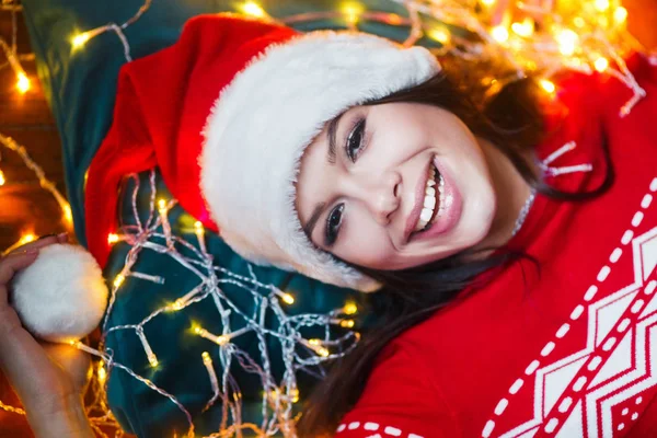 Retrato de cerca de la mujer envuelta en luces de Navidad acostada en el suelo en casa — Foto de Stock
