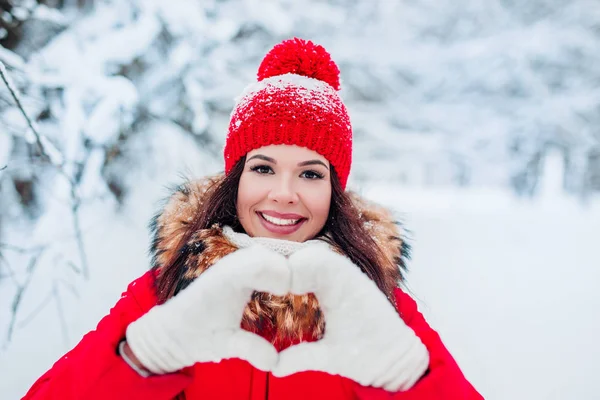 Mujer joven bastante romántica haciendo un gesto de corazón con los dedos delante de su pecho mostrando su amor en el fondo de invierno —  Fotos de Stock