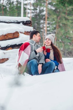 İle cups kar parkta oturan genç çift gülümsüyor. Eğleniyor sıcak içecekler içme.