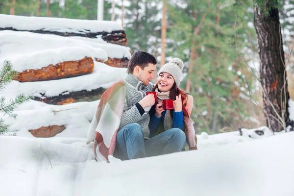 Casal jovem sorridente com copos sentados no parque de neve. Beber bebidas quentes, se divertir . — Fotografia de Stock